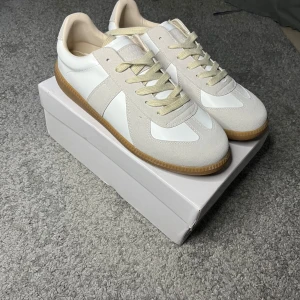 Maison Margiela GATs – 43  - Maison Margiela GATs – 43 👟 Stilrena och tidlösa sneakers från Maison Margiela – perfekt för både vardag och uppklätt. Vit/kräm i läder och mocka med klassisk gummisula.  • Storlek: EU 43 • Skick: Nyskick, endast testade inomhus • Nypris: ca 5000 kr • Medföljer: Originalkartong + dustbag.        Osäker på äkthet…. 💡 Köpta via Plick. Tidigare ägare uppgav att de är äkta och visade kvitto, men jag kan inte garantera äktheten – därav det låga priset.  