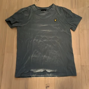 Blå T-shirt från Lyle & Scott Junior - Säljer en stilren blå t-shirt från Lyle & Scott Junior med klassisk gul logga broderad på bröstet. T-shirten har rund hals och korta ärmar, perfekt för en avslappnad look.