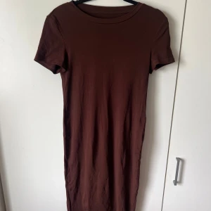 Brun t-shirtklänning - En enkel och stilren brun t-shirtklänning med rund halsringning och korta ärmar. Klänningen har en rak passform och är tillverkad i ett mjukt material som känns skönt mot huden. 