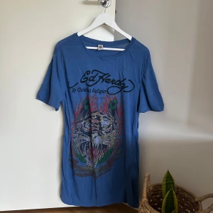 Blå Ed Hardy t-shirt -  t-shirt från Ed Hardy med stort färgglatt tryck och glittriga nitar framtill. T-shirten är i storlek L men har använts av mig xs/s som en översized t-shirt🫶