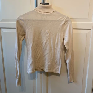 Beige polotröja från Prêt à Porter - Säljer en stilren beige polotröja från Prêt à Porter i storlek S. Tröjan har lång ärm och är tillverkad i ett mjukt, ribbat material vid kragen. Perfekt för lager-på-lager och enkel att matcha med olika outfits.