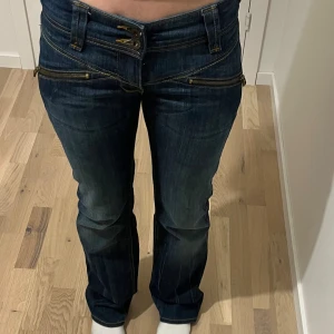 Mörkblå lågmidjade jeans med dragkedjedetaljer - Säljer ett par mörkblå jeans med låg midja och flera coola dragkedjor framtill. Jeansen är utsvängda och är från Levis. Säljer de på grund av att jag inte använder de längre 💕skriv gärna för frågor och kontakta innan ni köper!