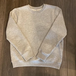 Ljusgrå sweatshirt från Kappahl - En stilren ljusgrå sweatshirt från Kappahl i mjuk bomulls- och polyestermix. Tröjan har rund halsringning, långa ärmar och ribbade muddar vid ärmslut och nederkant. Perfekt för en avslappnad och enkel look.