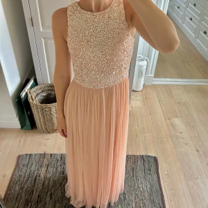 Långklänning från Lace & Beads - Säljer en elegant långklänning från Lace & Beads i champagnefärg/ rosa. Överdelen är täckt av pärlor och paljetter, medan kjolen är plisserad och faller mjukt. Klänningen är aldrig använd. Jag är 172 💕