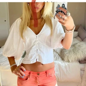 Vit blus med puffärmar och knappar - Säljer en söt vit blus med puffiga kortärmar och v-ringning. Blusen har knappar framtill, vilket ger en trendig look. Perfekt för varma dagar och enkel att matcha med olika nederdelar.