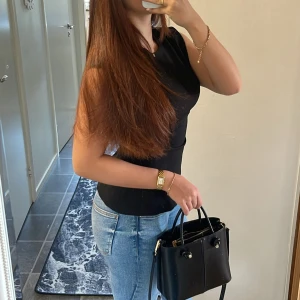 Svart figurnära topp - Säljer en svart, tight topp med korta ärmar och rund halsringning. Toppen har en enkel och stilren design som passar perfekt till jeans eller kjol. Materialet känns mjukt och följsamt mot kroppen. Lite slitet vid dragkedjan men det syns inte. 