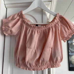 Ljusrosa croppad topp  - Säljer en ljusrosa croppad topp från H&M Divided. Toppen har korta puffärmar, resår vid halsringning och nederkant samt en lätt rynkad struktur. Perfekt för varma dagar och enkel att styla med kjol eller jeans.