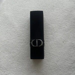 Dior Rouge läppstift 840 Rayonnante - Snyggt läppstift från Dior i nyansen 840 Rayonnante. Hylsan är svart med silverdetaljer och den klassiska CD-loggan. Färgen är en varm, bärig rödrosa ton som ger en lyxig känsla till läpparna.Kommer utan förpackning, oanvänd och otestad, om du köper fler av dessa läppstift kan jag tänka mig bättre pris. Rensning inför flytt. Vissa märken på själva skalet på läppstiftet då jag förvarat alla i samma låda 