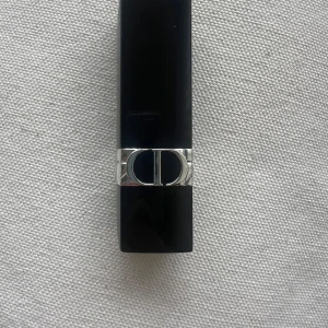 Rouge Dior läppstift 762 Dioramour Metallic - Rouge Dior läppstift i nyansen 762 Dioramour Metallic. Färgen är en djup röd med metallisk finish. Hylsan är svart med silverdetaljer och Dior-logga. Lyxig och klassisk design, perfekt för att ge läpparna en elegant touch. Kommer utan förpackning, oanvänd och otestad, om du köper fler av dessa läppstift kan jag tänka mig bättre pris. Rensning inför flytt. Vissa märken på själva skalet på läppstiftet kan förekomma då jag förvarat alla i samma låda 