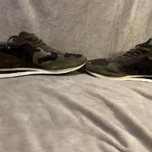  Philippe Model - Säljer ett par snygga sneakers från Philippe Model i kamouflagefärgat mönster med gröna och bruna toner. Skorna har snörning, rund tå och detaljer i mocka. Perfekta för dig som vill sticka ut med en sportig och trendig look.46 9/10 skick två små defekter men syns inte 
