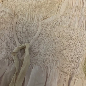 Ljusrosa blus från Odd Molly - Supersöt ljusrosa blus från Odd Molly med smockdetaljer över byst och rygg, v-ringning och knytband framtill. Långa ärmar och lätt, luftig bomullskvalitet. Perfekt för en sommar kväll