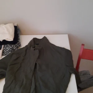 Mörkgrön linneskjorta med ståkrage - Säljer en mörkgrön skjorta i linne med ståkrage och lång ärm. Skjortan har en avslappnad passform och knäppning framtill. Perfekt för dig som gillar en stilren och enkel look.