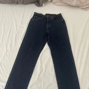 Levi's 501 mörkblå jeans - Klassiska Levi's 501 jeans i mörkblå denim med raka ben och femficksmodell. Byxorna har knappgylf och tydliga Levi's-detaljer som läderpatch bak och logotyp på fickan. Perfekta för dig som gillar tidlös stil.