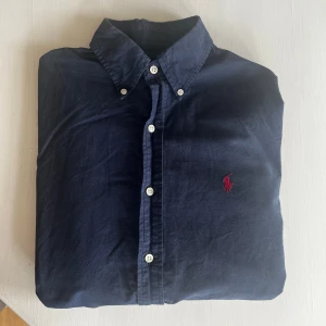Mörkblå skjorta från Ralph Lauren - Klassisk mörkblå skjorta från Ralph lauren. perfekt för en stilren look. Skick 8/10 bara lite skrynklig men går över med en strykning. Storlek S.