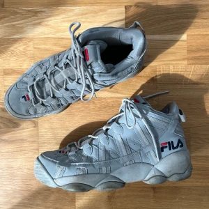 Grå Fila sneakers med hög sula - Säljer ett par grå Fila sneakers med hög sula och tydlig logga på sidan. Skorna har snörning och är tillverkade i syntetmaterial. Perfekta för dig som gillar chunky sneakers med sportig vibe.