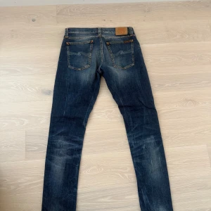 Nudie Jeans Tight Long John Org. - Säljer ett par Nudie Jeans Tight Long John i färgen Org. Grey Blues. Jeansen är slim fit med låg midja och tillverkade av 98% ekologisk bomull och 2% elastan. Klassisk femficksmodell med orangea sömmar och snygg tvätt.