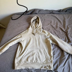 Beige hoodie med ficka framtill - Säljer en beige hoodie med huva och känguruficka framtill. Tröjan har långa ärmar och ribbade muddar vid ärmslut och nederkant. Perfekt för en avslappnad stil.