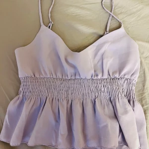 Ljuslila linnetopp med smock - Säljer en ljuslila linnetopp med smala axelband och smockad midja. Toppen har en volangig nederdel 💕
