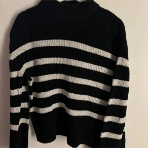 Svartvit randig stickad tröja - Säljer en svart stickad tröja med vita ränder. Tröjan har lång ärm och en något högre hals. Fint skick! Storlek S/M