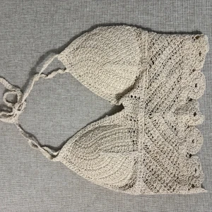 Beige virkad topp - Säljer en beige virkad topp med knyt i nacken och ryggen. Toppen har en fin spetsliknande kant och vadderade kupor för extra komfort. Perfekt för sommardagar på stranden.