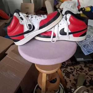 Nike Air Jordans i rött, vitt och svart - Säljer ett par klassiska Nike Air Jordans high-top sneakers i rött, vitt och svart. Skorna har svart swoosh, vit sula och röda paneler i skinn. Perfekta för dig som gillar streetwear och vill sticka ut med en ikonisk modell.