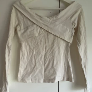 Vit omlottopp från Bik Bok - Säljer en vit långärmad topp från Bik Bok med snygg omlottdetalj över axlarna. Toppen har en bred, v-ringad offshoulder-ringning och är tillverkad i bomull med lite stretch för en bekväm passform.