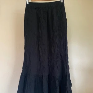 Svart långkjol med volang - Säljer en svart långkjol med volang nertill. Kjolen har en lätt skrynklig struktur och är perfekt för dig som gillar en enkel men ändå stilren look. Passar till många olika outfits och är superenkel att matcha.