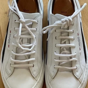 Hugo Boss herrsneakers i stl. 42 - Hugo Boss herrsneakers i stl. 42 i vitskinn med blå detaljer. Skorna har använts ett par gånger och är i mycket gott skick. Pris 1000kr plus porto.