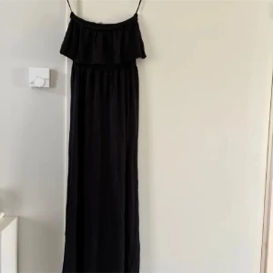 Svart långklänning med volang  - Svart långklänning från Gina Tricot med smala axelband och volang upptill. Klänningen har en luftig passform och är perfekt för varma dagar. Enkel och stilren design som passar till många tillfällen.