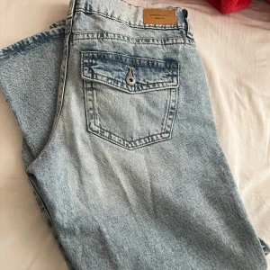 Ljusblå jeansbyxor från Gina Tricot - Säljer ett par ljusblå jeansbyxor från Gina Tricot med klassisk femficksdesign och knappgylf. Jeansen har raka ben och normal passform, samt en snygg tvättad look. Perfekta för en avslappnad stil.