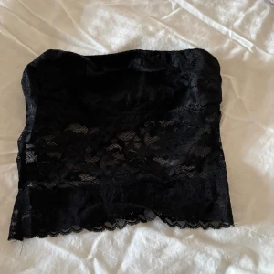 Svart spets tubtopp - Säljer en svart tubtopp i spets med fina blommiga detaljer. Toppen är axelbandslös och har en elastisk kant upptill för bättre passform. 