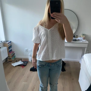 Vit blus med broderade blommor - Säljer en söt vit blus med korta puffärmar och v-ringning. Blusen har broderade blommor och knappar framtill. Perfekt för dig som gillar romantisk och luftig stil.