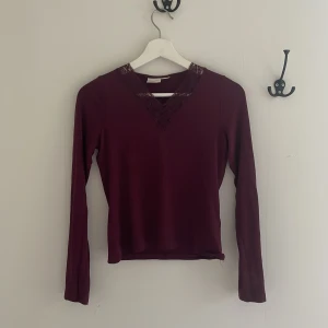 Vinröd långärmad topp med spets från Gina Tricot - Säljer en vinröd långärmad topp från Gina Tricot med v-ringning och spetsdetaljer vid halsen. Tunn och mjuk i materialet, perfekt för lager-på-lager eller som den är.