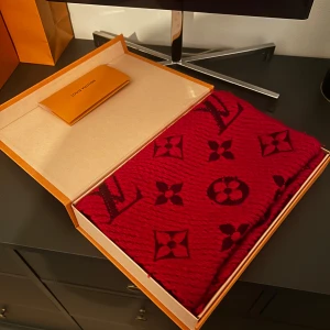 Louis Vuitton halsduk  - Säljer en lyxig röd halsduk från Louis Vuitton med ikoniskt monogrammönster i mörkrött. Halsduken är stickad och kommer med originalförpackning och kvitto. Den är köpt inne vid Louis Vuitton butiken i Stockholm. Perfekt accessoar för att lyfta din outfit.