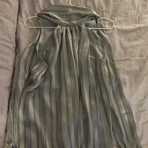 Blå randig halterneck topp - Säljer en elegant blå halterneck topp  med tunna vertikala ränder och transparent, lätt material. Toppen har långa ärmar och ett luftigt fall, perfekt för dig som gillar en stilren look.