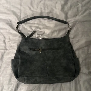 Mörkgrå axelväska med avtagbar rem - Aldrig användt väskan. Säljer en stilren mörkgrå axelväska med flera dragkedjefickor och avtagbar axelrem. Väskan har både kortare handtag och en längre justerbar rem som kan tas av. Perfekt för dig som vill ha en praktisk och snygg accessoar.