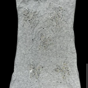 Grå vintage tubtopp med spets och pärlor från 2000s  - Grå ribbad tubtopp dekorerad med pärlor och glittriga detaljer framtill. Baksidan har en bred spetspanel med små pärlor och blommönster. Perfekt för att addera lite extra till din outfit.