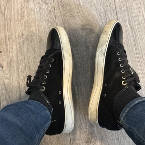 Svarta sneakers med vit sula - Svarta sneakers med vit platt sula och svarta skosnören. Ovandelen är i mocka och tån är rund. Skorna har metallfärgade öljetter och en stilren design som passar till mycket.