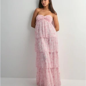 Ljusrosa klänning med volanger - Super fin ljusrosa balklänning med blomdetaljer! Klänningen är axelbandslös men kan även bäras med halterneckband. Perfekt för sommarens speciella tillfällen. Aldrig använd då den var för lång för mig (är 156cm) nypris 699kr 