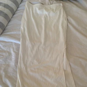 Vit ribbad långkjol med slits - Säljer en stilren vit långkjol med ribbad struktur och en snygg slits på sidan. Kjolen har en rak och tight passform och är perfekt för dig som gillar minimalistisk stil. Superenkel att matcha med olika toppar! 