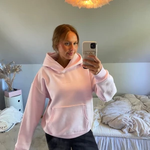 Ljusrosa hoodie från Caspara - Säljer en ljusrosa hoodie från Caspara med broderad logga på bröstet. Tröjan har huva, magficka och ribbade muddar. Perfekt för en avslappnad stil och riktigt mjuk insida.