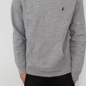 Grå hoodie från Ralph Lauren - (Original pris 1500)Säljer en klassisk grå hoodie från Ralph Lauren med broderad blå logga på bröstet. Tröjan har huva, känguruficka och ribbade muddar. Perfekt för en avslappnad stil.