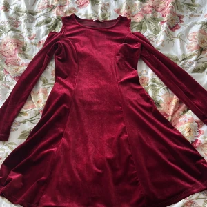 Vinröd sammetsklänning med lång ärm och cold shoulder detalj.  - Vinröd sammetsklänning från Cubus med lång ärm och cold shoulder-detalj. Klänningen har en lätt utsvängd kjol och rund halsringning. Perfekt för dig som gillar en elegant och mjuk känsla.
