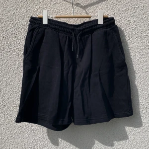 Svarta shorts från Weekday med dragsko - Svarta shorts från Weekday med elastisk midja och dragsko. Modellen har sidofickor och en bakficka. Tillverkade i mjuk bomullsblandning med polyester. Korta ben med klassisk passform.