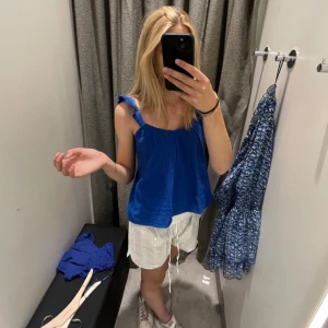 Blå linnetopp med volangaxelband - Säljer en blå linnetopp med volangdetaljer på axelbanden. Toppen har en lös passform och är ärmlös, perfekt för varma dagar. Enkel och stilren design som passar till mycket.