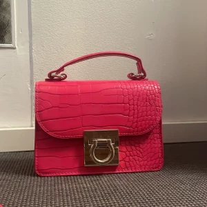 Rosa axelväska med krokodilpräglat mönster - En snygg rosa axelväska med krokodilpräglat mönster. Ett långt band finns med. Fint skick