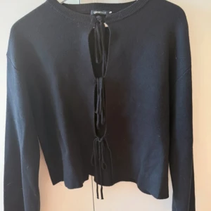 Svart stickad tröja med snörning från Gina Tricot - Svart stickad tröja från Gina Tricot med lång ärm och snygg snörningsdetalj framtill. Tröjan har en croppad passform och rund halsringning 🩷