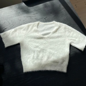 Vit fluffig croppad tröja - Supermjuk och fluffig vit tröja med korta ärmar och v-ringning. Croppad modell som passar perfekt till höstens och vinterns outfits. Tröjan har en mysig känsla och är lätt att matcha med olika stilar.