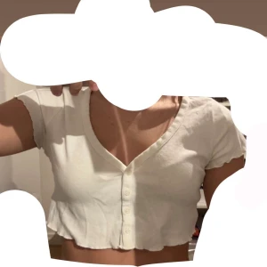 Vit topp med knappar H&M - Säljer en vit croppad topp från H&M med korta ärmar och v-ringning. Toppen har knappar framtill och är i mjukt bomullsmaterial. Perfekt till sommaren och enkel att matcha med jeans eller kjol eller när man sover. Använd ca 5 gånger. Passar XS, S och M. 
