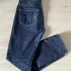 Levi's 501 mörkblå jeans - Klassiska Levi's 501 jeans i mörkblå denim. Rak passform med fem fickor och knappgylf. Perfekta för dig som gillar tidlös stil och vill ha ett par jeans som funkar till det mesta. Pris ej hugget i sten. L32 W32